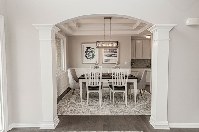 dining space with a raised ceiling, dark wood finished floors, and ornate columns