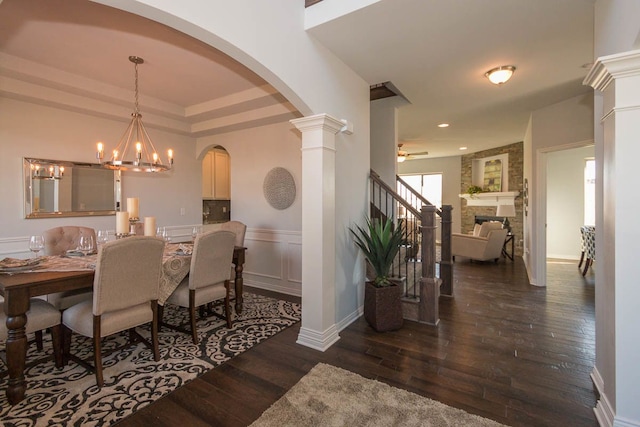 dining room featuring arched walkways, wood-type flooring, a chandelier, a stone fireplace, and ceiling fan
