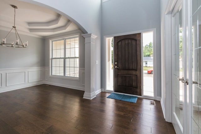 foyer entrance with arched walkways, dark wood-style floors, a raised ceiling, a chandelier, and wainscoting