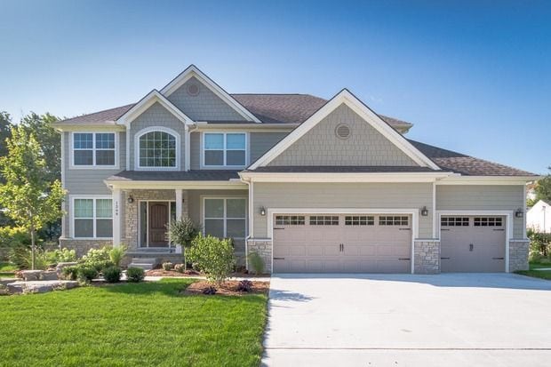 craftsman house featuring a garage, stone siding, driveway, a front yard, and covered porch