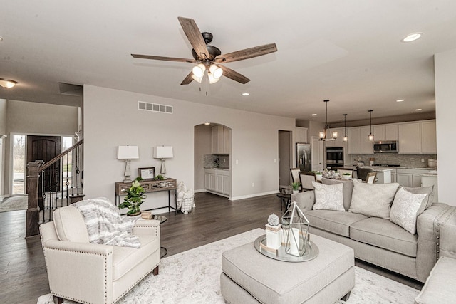 living room with arched walkways, a ceiling fan, wood finished floors, baseboards, and stairway