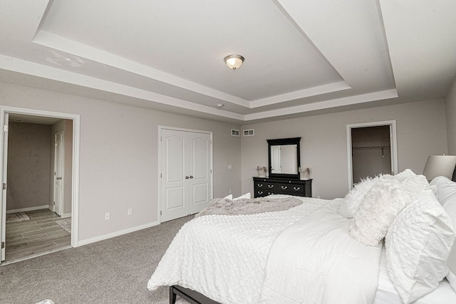 carpeted bedroom with a raised ceiling, baseboards, a closet, and ensuite bathroom