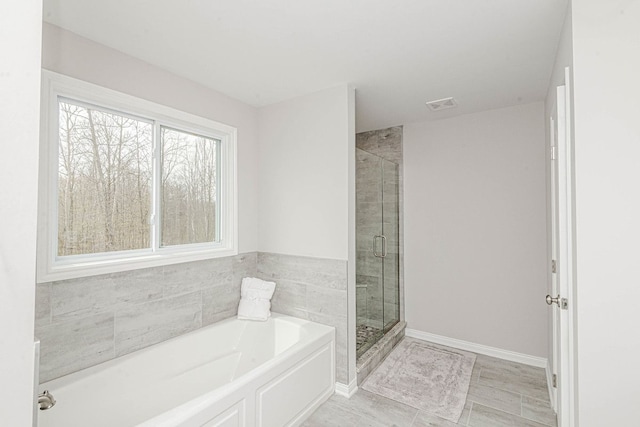 bathroom with a stall shower, a bath, and baseboards