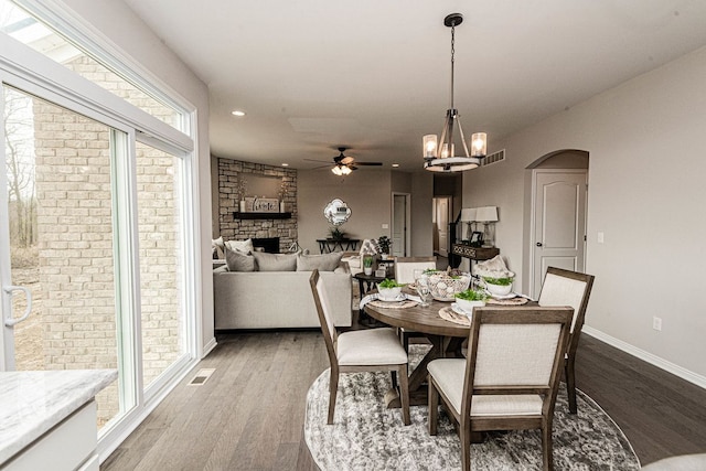 dining space with a ceiling fan, wood finished floors, a stone fireplace, baseboards, and recessed lighting