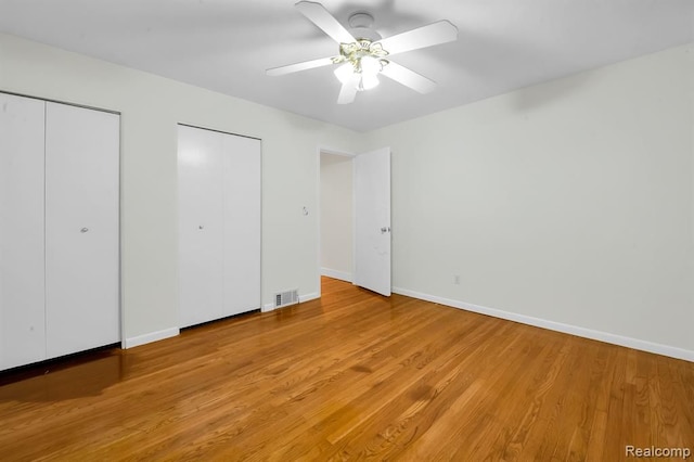 unfurnished bedroom featuring two closets, light wood-style floors, baseboards, and a ceiling fan