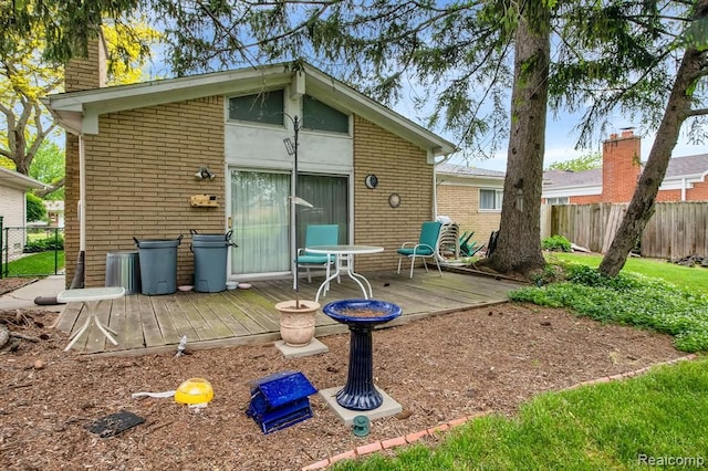 back of property with fence, a wooden deck, and brick siding
