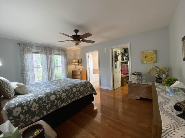 bedroom with wood finished floors, a walk in closet, baseboards, a closet, and ensuite bath
