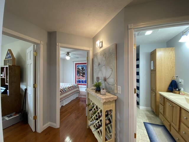 ensuite bathroom featuring baseboards, vanity, wood finished floors, a textured ceiling, and ceiling fan