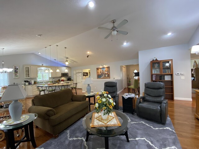 living room with vaulted ceiling, ceiling fan, wood finished floors, baseboards, and a chandelier