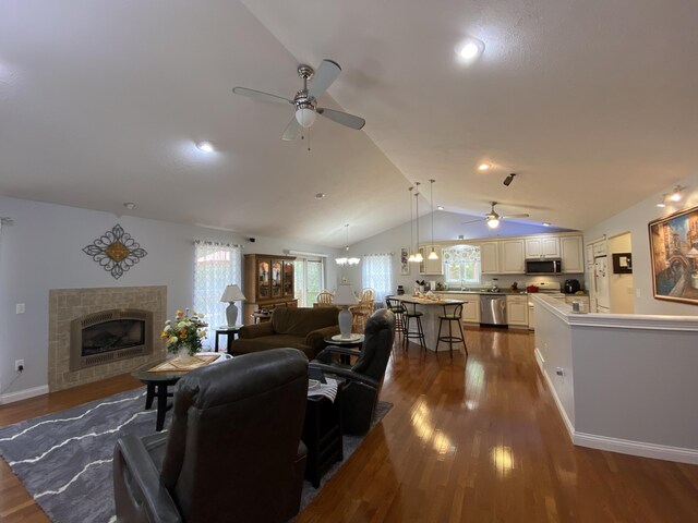 living room with a ceiling fan, vaulted ceiling, dark wood finished floors, a fireplace, and baseboards