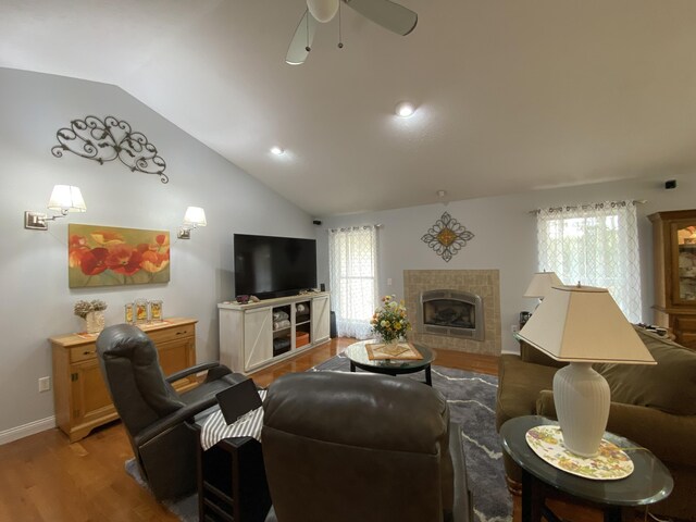 living room with wood finished floors, vaulted ceiling, a ceiling fan, a tile fireplace, and baseboards