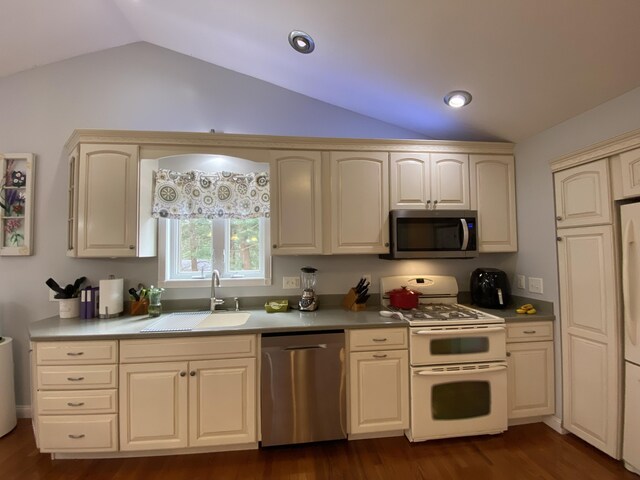 kitchen featuring stainless steel appliances, a sink, vaulted ceiling, dark wood-style floors, and cream cabinetry