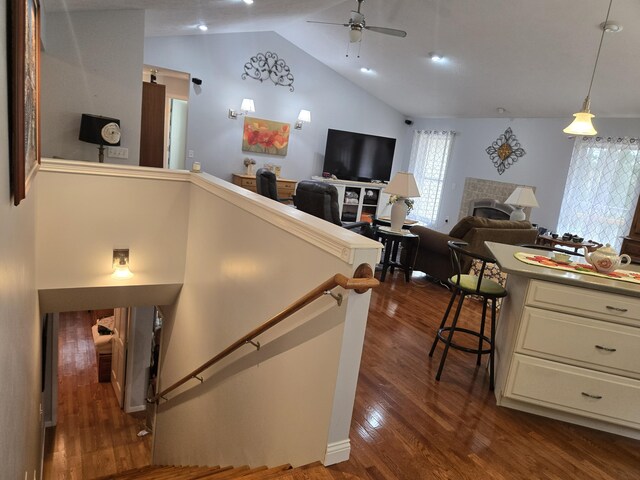 stairs with wood finished floors, lofted ceiling, a ceiling fan, and a tile fireplace