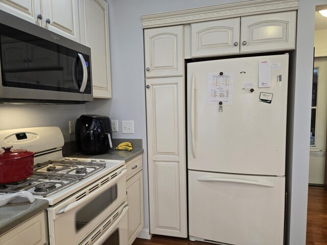kitchen with white appliances, cream cabinetry, dark wood-style floors, and dark countertops