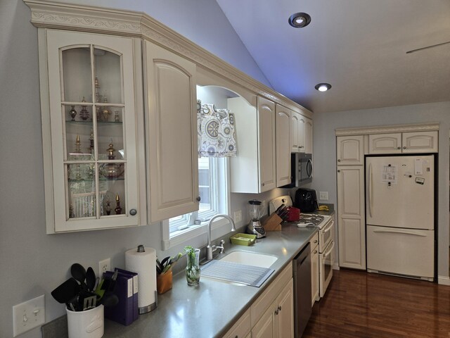 kitchen featuring appliances with stainless steel finishes, a sink, glass insert cabinets, dark wood-style flooring, and vaulted ceiling