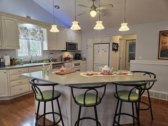 kitchen with appliances with stainless steel finishes, vaulted ceiling, a kitchen breakfast bar, a sink, and dark wood finished floors