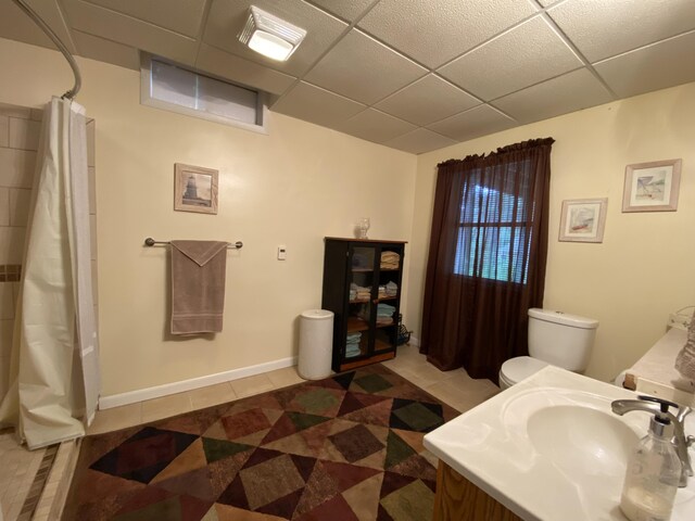 full bathroom featuring a paneled ceiling, tile patterned flooring, a sink, curtained shower, and toilet