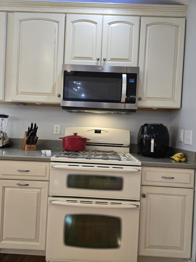 kitchen with stainless steel microwave, range with two ovens, dark countertops, and cream cabinets