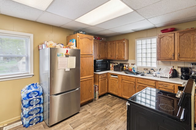kitchen with black appliances, light wood-style floors, brown cabinets, a paneled ceiling, and light countertops