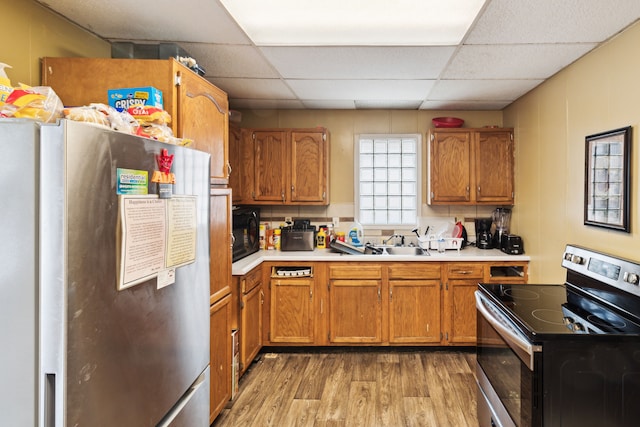 kitchen with appliances with stainless steel finishes, light wood-type flooring, a paneled ceiling, light countertops, and brown cabinetry