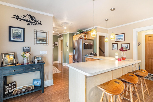 kitchen with stainless steel fridge with ice dispenser, crown molding, wood finished floors, a peninsula, and a kitchen breakfast bar