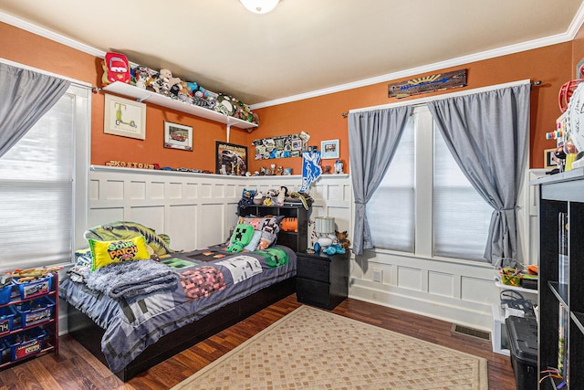 bedroom with multiple windows, crown molding, wood finished floors, a decorative wall, and a wainscoted wall