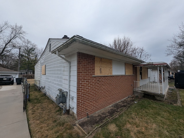 view of side of property with brick siding, a lawn, and covered porch