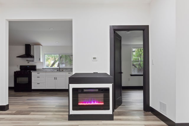19178 Sherwood St, Detroit, MI 48234 - kitchen featuring black gas stove, wall chimney range hood, white cabinetry, a sink, and light wood-style flooring