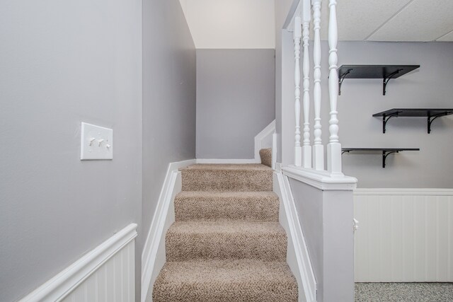 stairway featuring a wainscoted wall and carpet