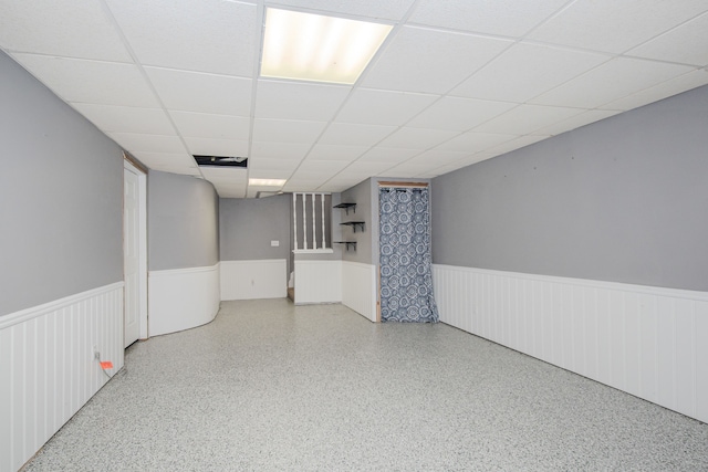finished basement featuring a wainscoted wall and a paneled ceiling