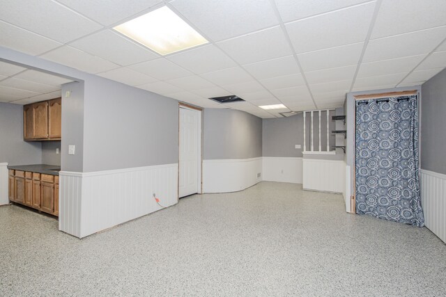 finished below grade area featuring a wainscoted wall and a drop ceiling