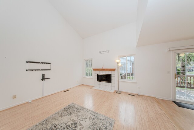 unfurnished living room featuring high vaulted ceiling, wood finished floors, baseboards, and a tile fireplace