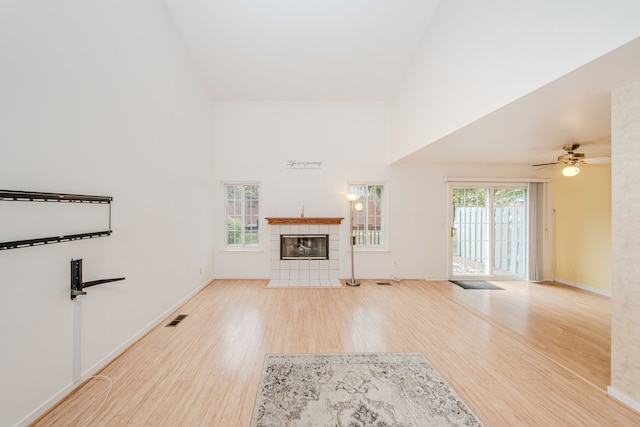 unfurnished living room with a tiled fireplace, a towering ceiling, wood finished floors, baseboards, and a ceiling fan