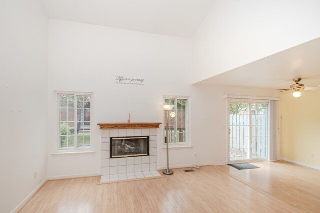 unfurnished living room with a high ceiling, wood finished floors, a tile fireplace, baseboards, and a ceiling fan