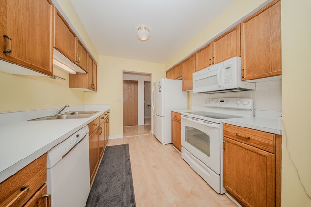 kitchen featuring white appliances, light wood finished floors, light countertops, a sink, and brown cabinets