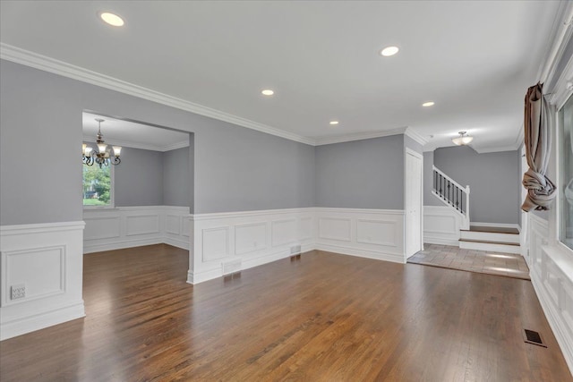 unfurnished living room featuring a chandelier, stairway, wood finished floors, wainscoting, and a decorative wall