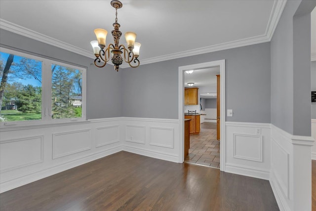 unfurnished dining area featuring a chandelier, a wainscoted wall, dark wood-type flooring, and ornamental molding