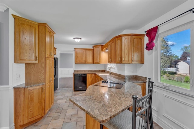 kitchen featuring black appliances, a kitchen bar, a sink, a peninsula, and light stone countertops