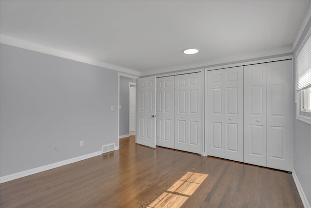 unfurnished bedroom with two closets, wood finished floors, and baseboards