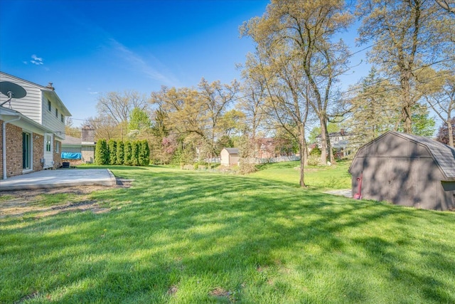 view of green lawn featuring a storage unit, a patio, and an outbuilding