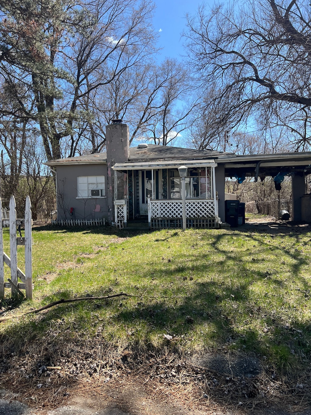 ranch-style home featuring a chimney, a front yard, a carport, and a porch