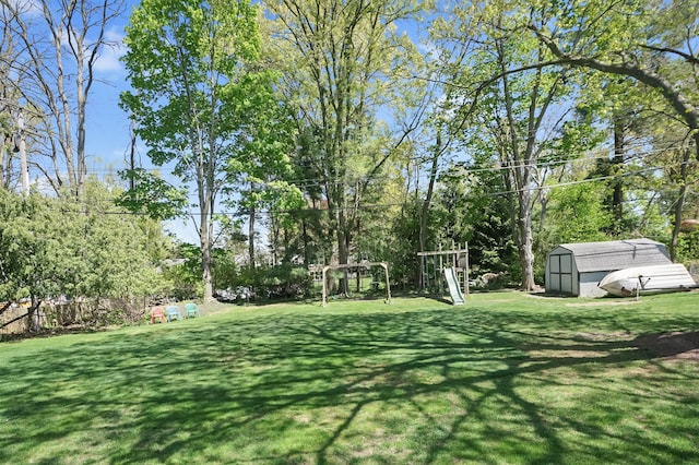 view of green lawn featuring a storage shed, a playground, an outdoor structure, and view of wooded area