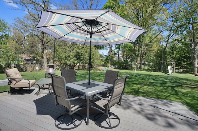 deck featuring outdoor dining area, a lawn, and view of wooded area