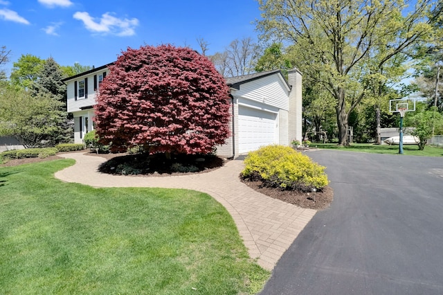 view of side of home featuring driveway, a chimney, a lawn, and a garage