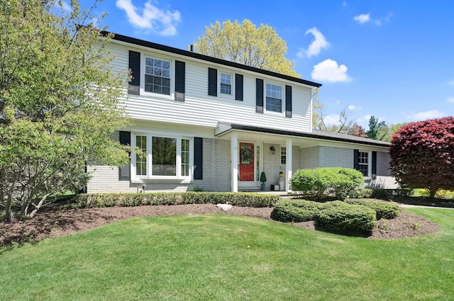 view of front of house featuring a front yard, brick siding, and covered porch