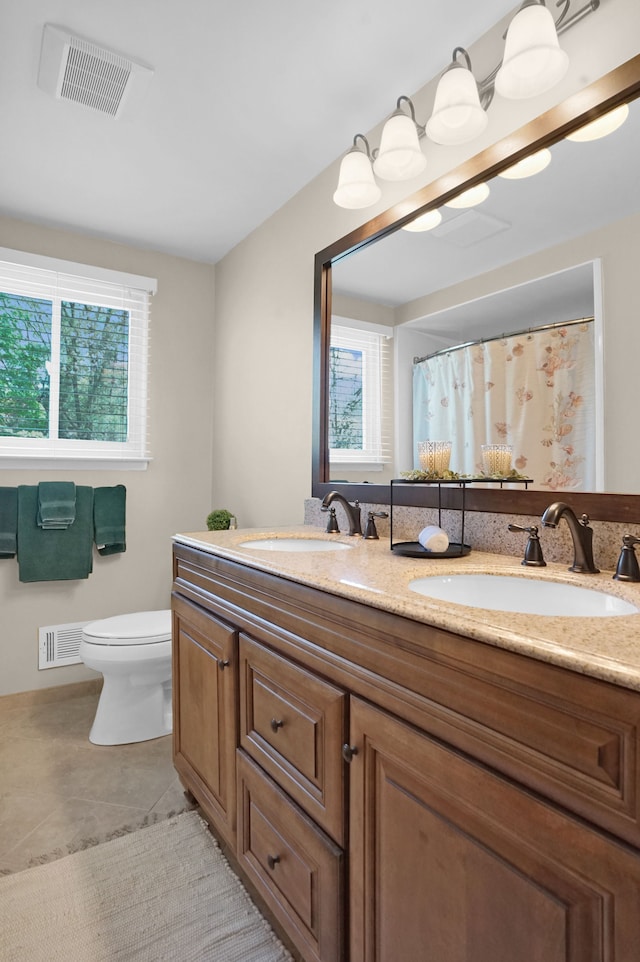 full bathroom featuring healthy amount of natural light, toilet, double vanity, and tile patterned floors