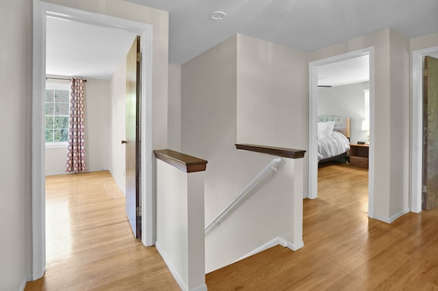 hall with an upstairs landing, light wood finished floors, and baseboards