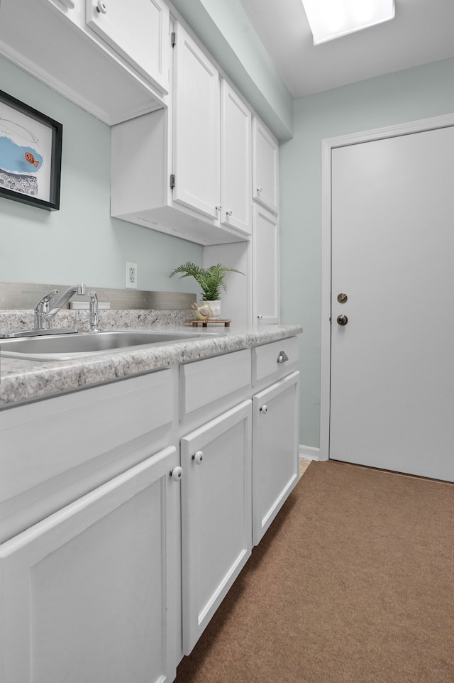 kitchen with dark colored carpet, white cabinets, light countertops, and a sink