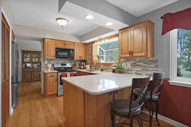 kitchen with stainless steel appliances, a sink, a peninsula, light countertops, and tasteful backsplash
