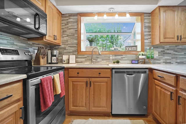 kitchen featuring appliances with stainless steel finishes, a sink, light countertops, tasteful backsplash, and light wood-style floors